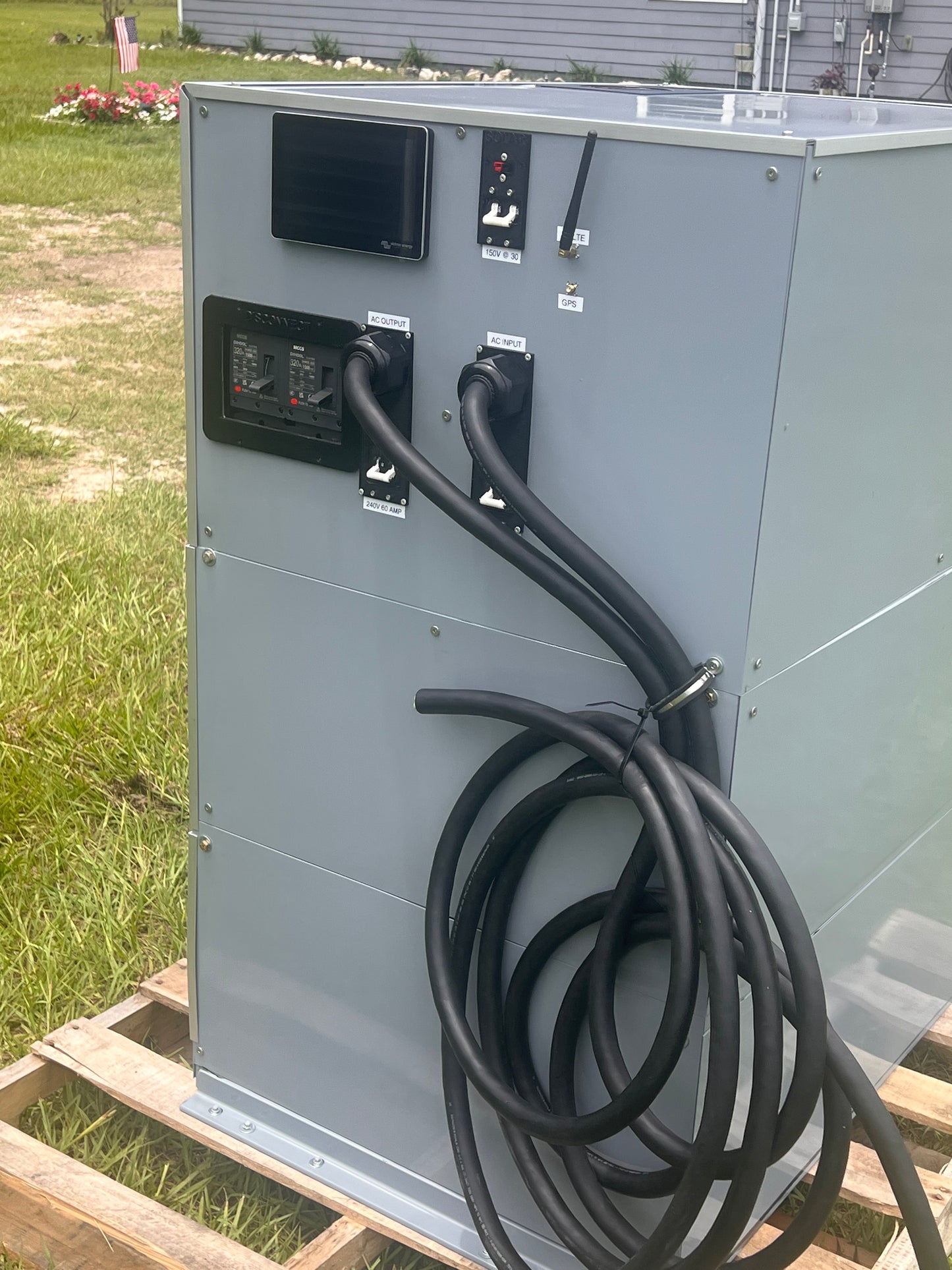 Electrical panel with a coiled black cable on a grassy outdoor area